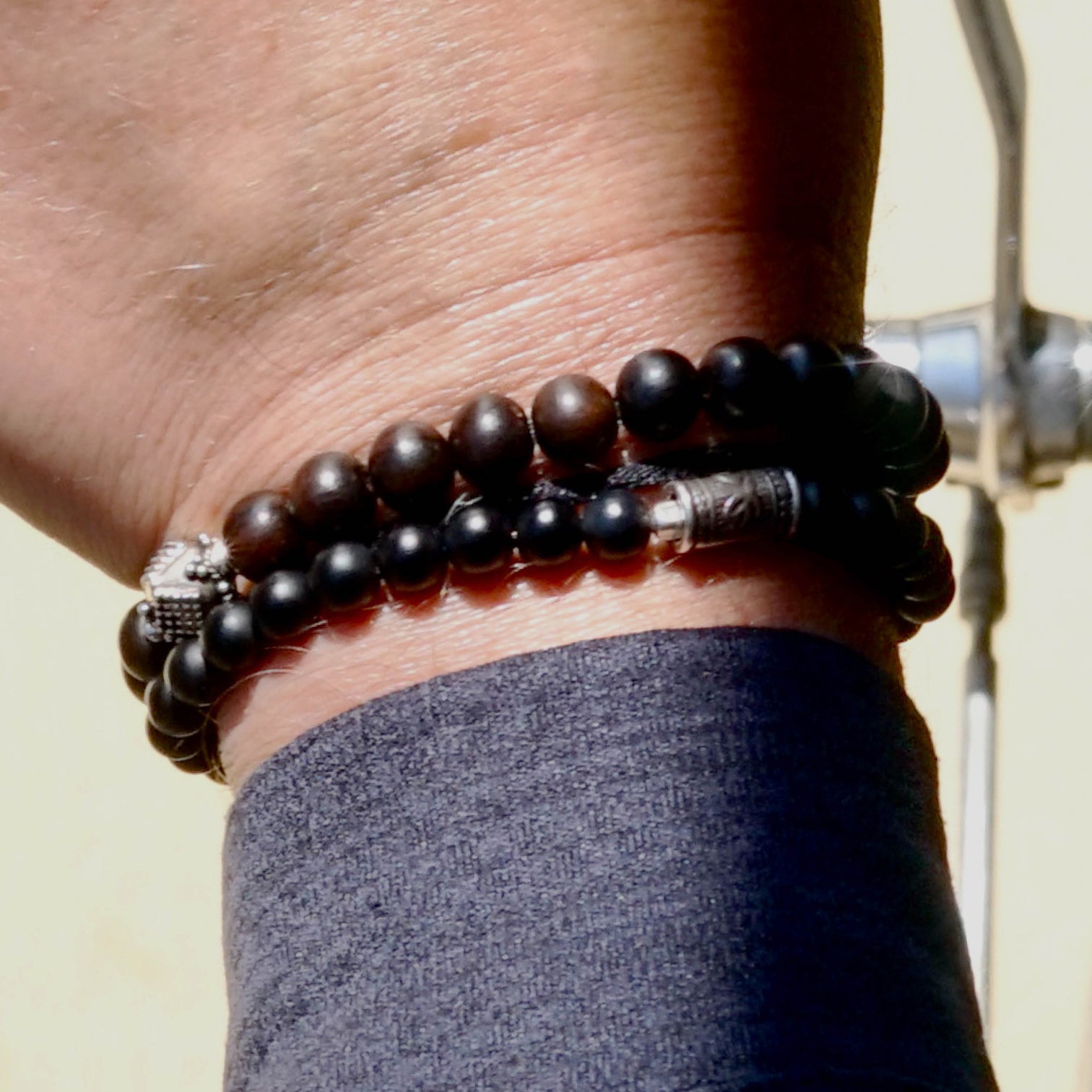 Detail shot of a male model 's wrist. He is wearing the ALEC Men beaded bracelet made with Ebony and a sterling silver center piece and the MAXIM Men beaded bracelet made with Mat Black Onyx and sterling silver elements.