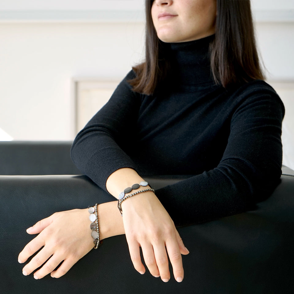 Picture of a female model.  The upper part of her body withouth the eyes is visible. She is wearing the ELEA Double Wrap Bracelet made with Mother of Pearl and Pyrite.