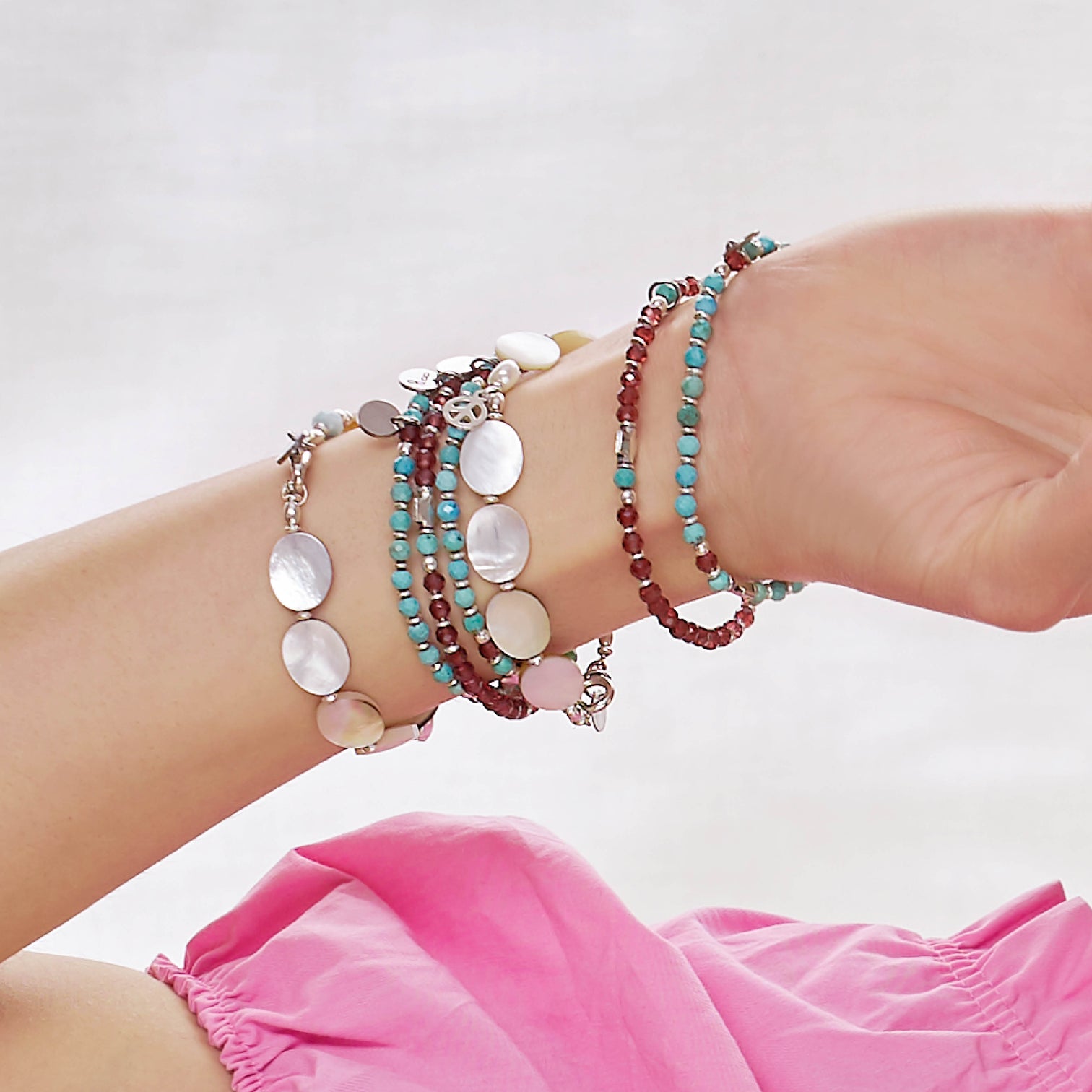 Detail of a female Model 's wrist wearing the Kya Bracelet made with Turquoise, and Garnet , the Sia Bracelet made with Garnet and Turquoise and the Marilla Bracelet made with Mother of Pearl.