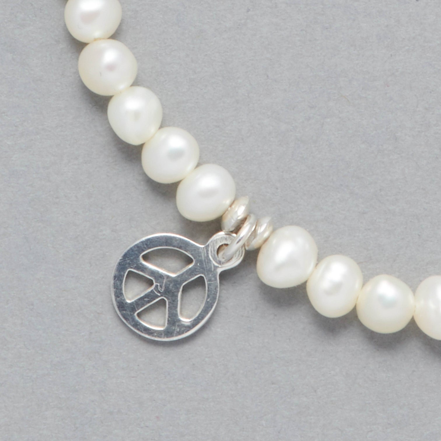 Detail Shot of the Marina Bracelet made with Cultured Freshwater white Pearls and a Sterling Silver Peace Symbol Charm. 