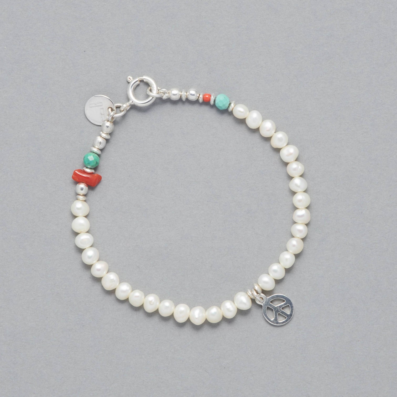 Product shot of the Marina Bracelet made with Cultured Freshwater white Pearls, faceted Turquoise, Sterling Silver Elements and a Peace Symbol Sterling Silver Peace Symbol Charm.