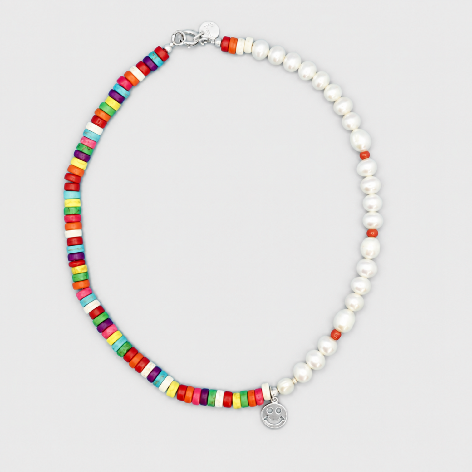  ALEGRIA necklace with white pearls, multicoloured disc beads, corald beads, a smiley pendant and clasp on a light grey background.