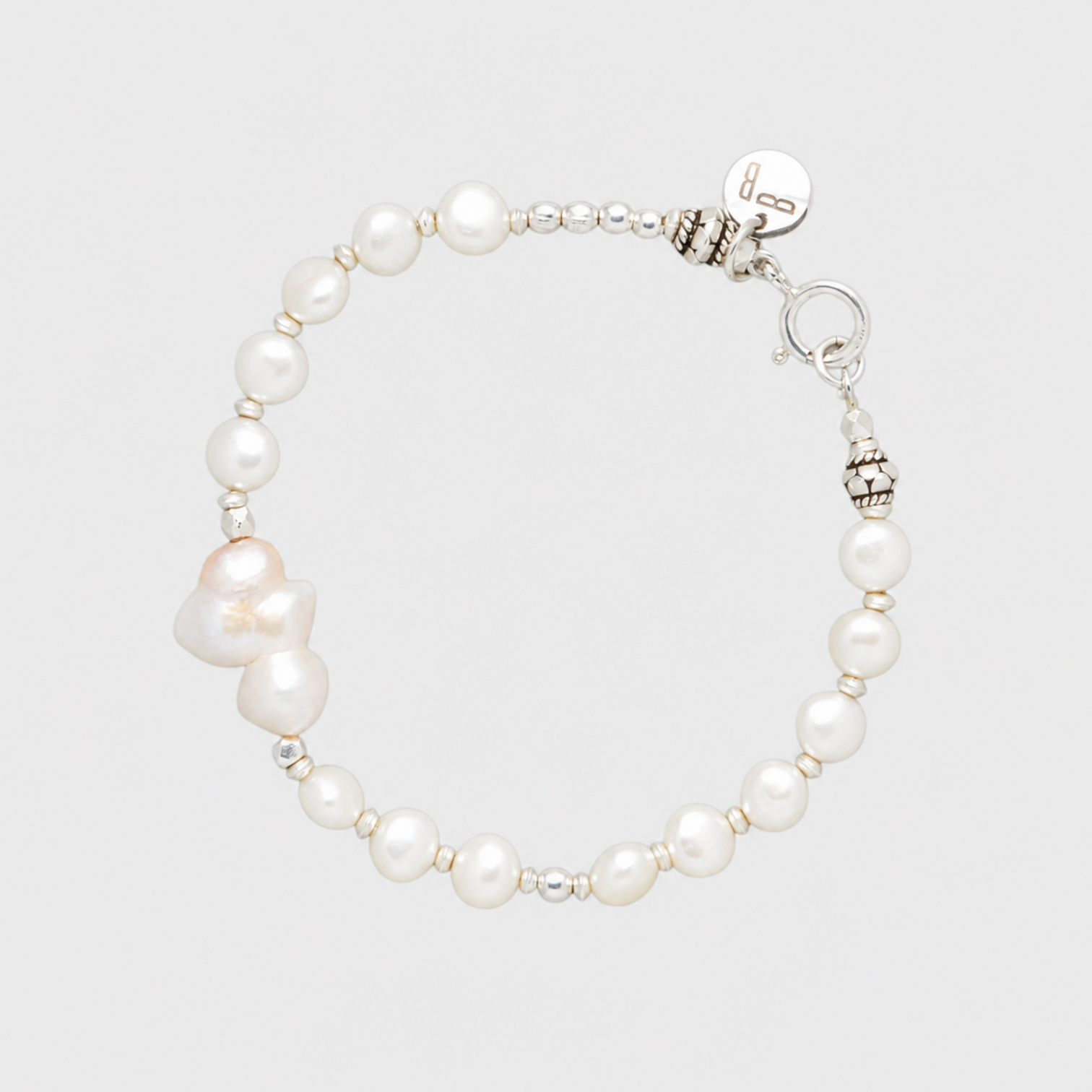 BIANCA white pearl bracelet with irregular pearls, silver-tone spacers, clasp and round tag on a light grey background.