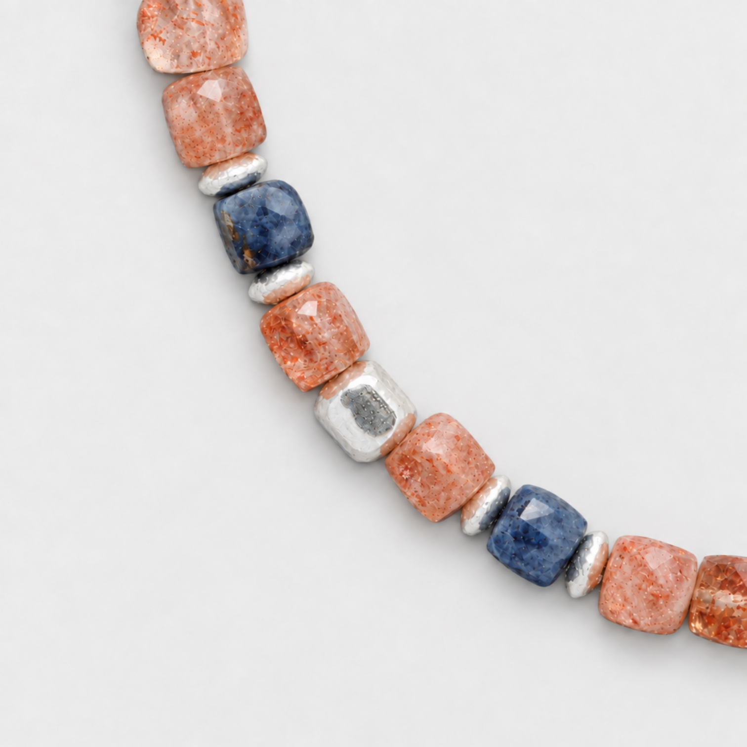Close-up of the sunstones, blue sapphires and sterling silver element on a neutral light-grey background.