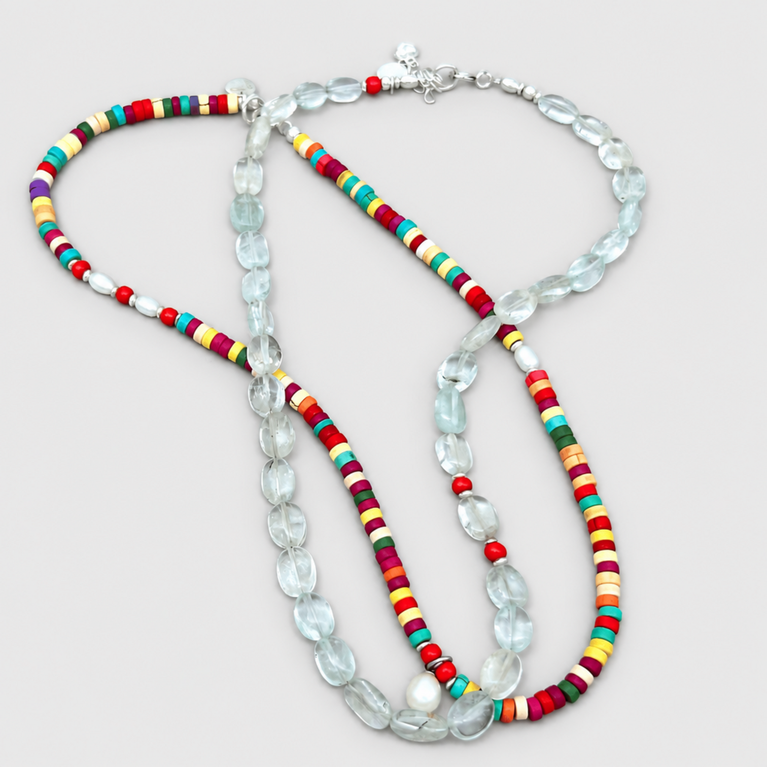 GEMMA aquamarine and coral necklace overlapping a multicoloured beaded necklace on a neutral light-grey background.
