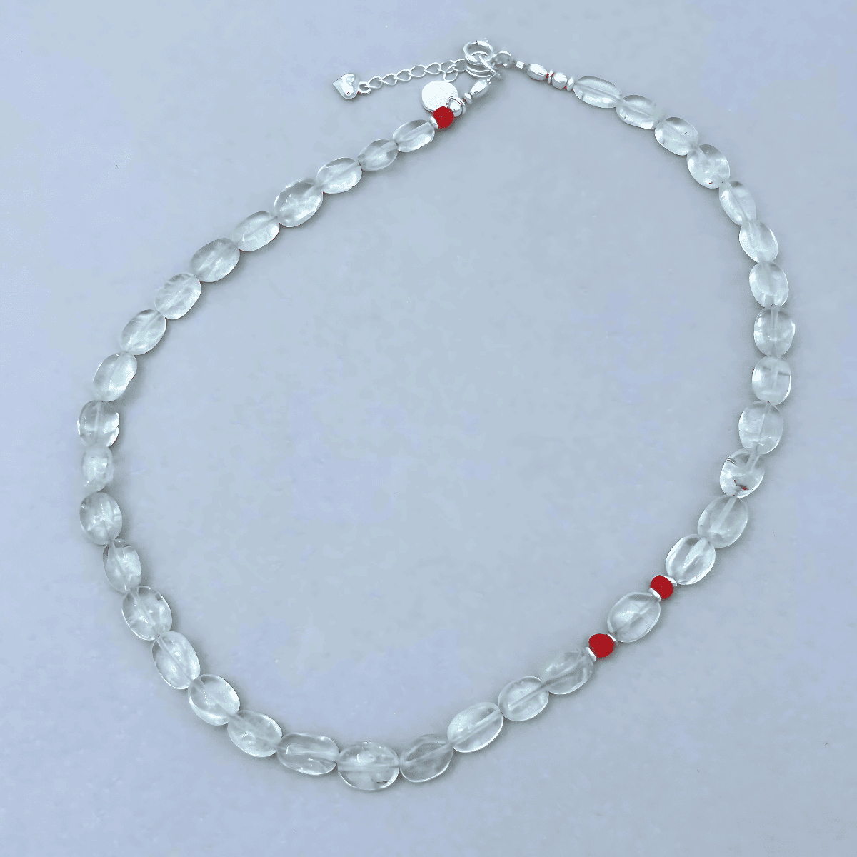 A beaded necklace made of oval Aquamarine beads with three small red coral accent beads and a silver clasp, displayed on a light gray background.