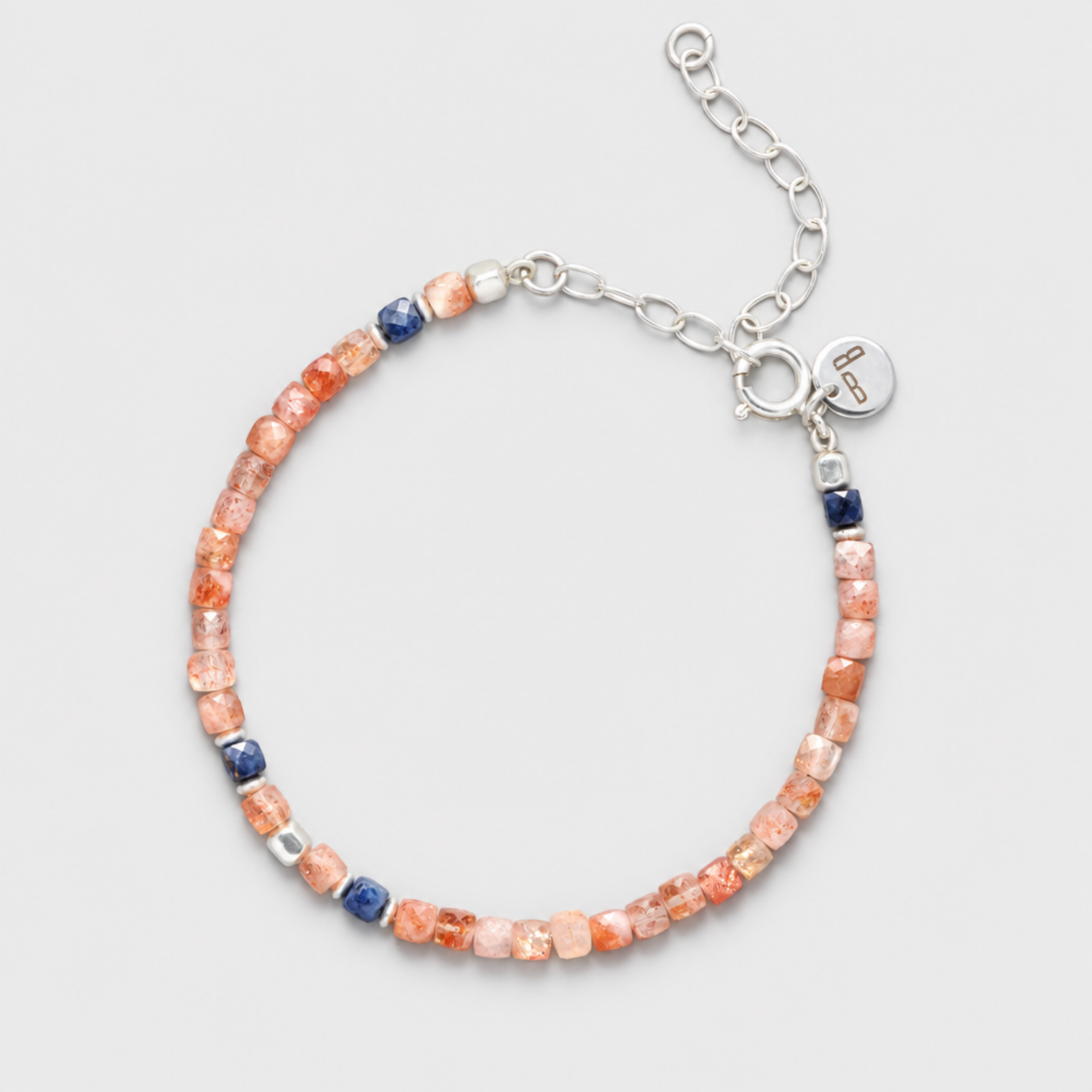 GINGER anklet with peach sunstones, blue sapphires, sterling silver clasp, round charm and extension chain on a neutral light-grey background.
