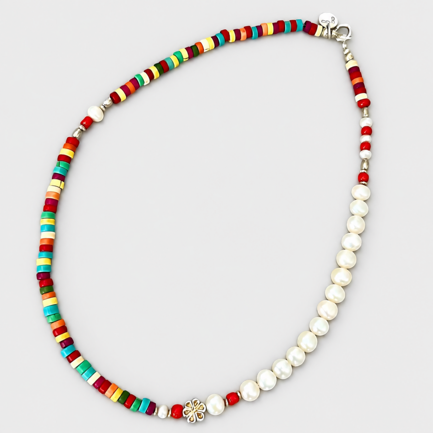 HAPPY necklace with white pearls, multicoloured disc beads, corald beads, a silver flower detail and clasp on a light grey background.