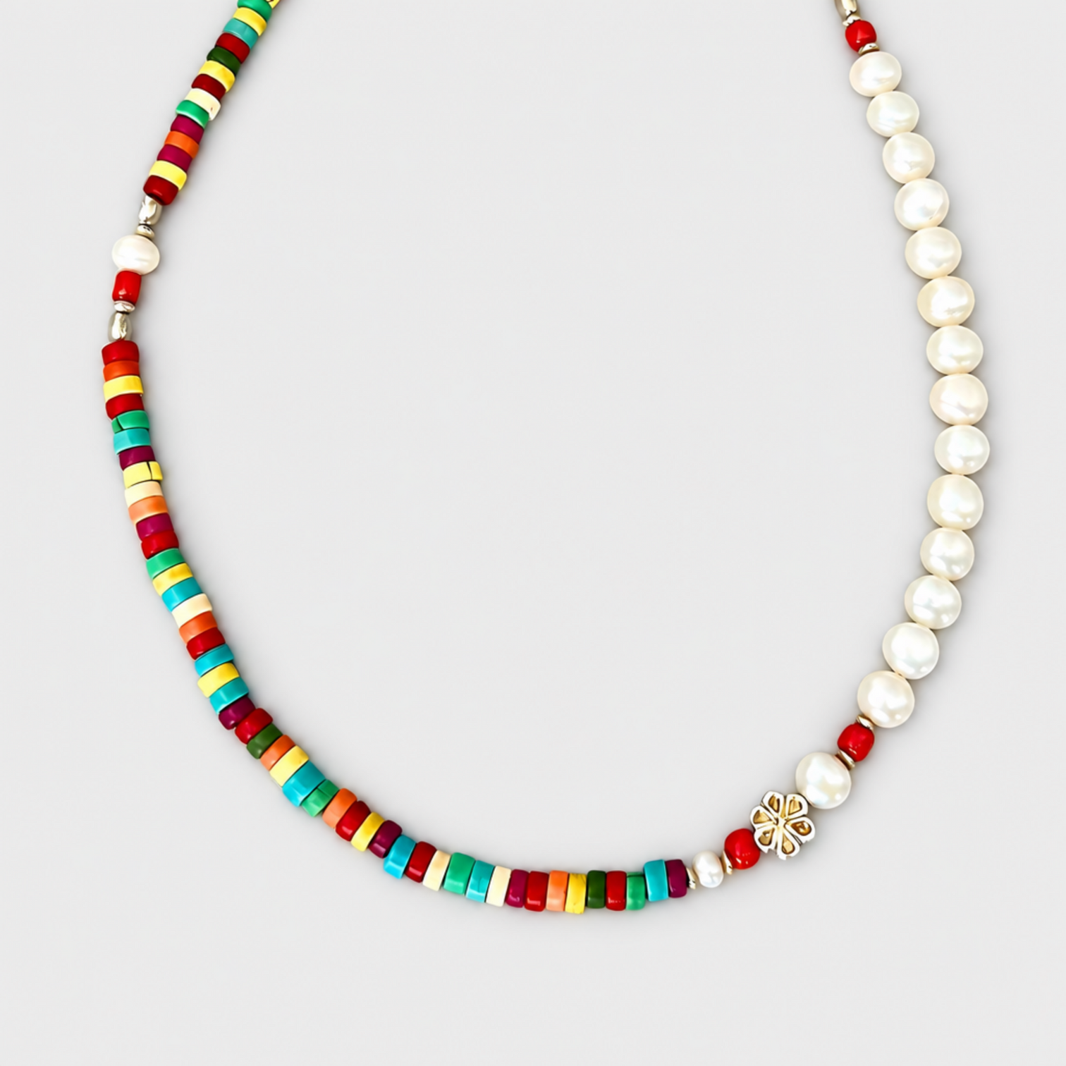 Close-up of the HAPPY necklace is made with multicoloured discs, white pearls,corald accent beads and a silver flower detail on a light grey background.