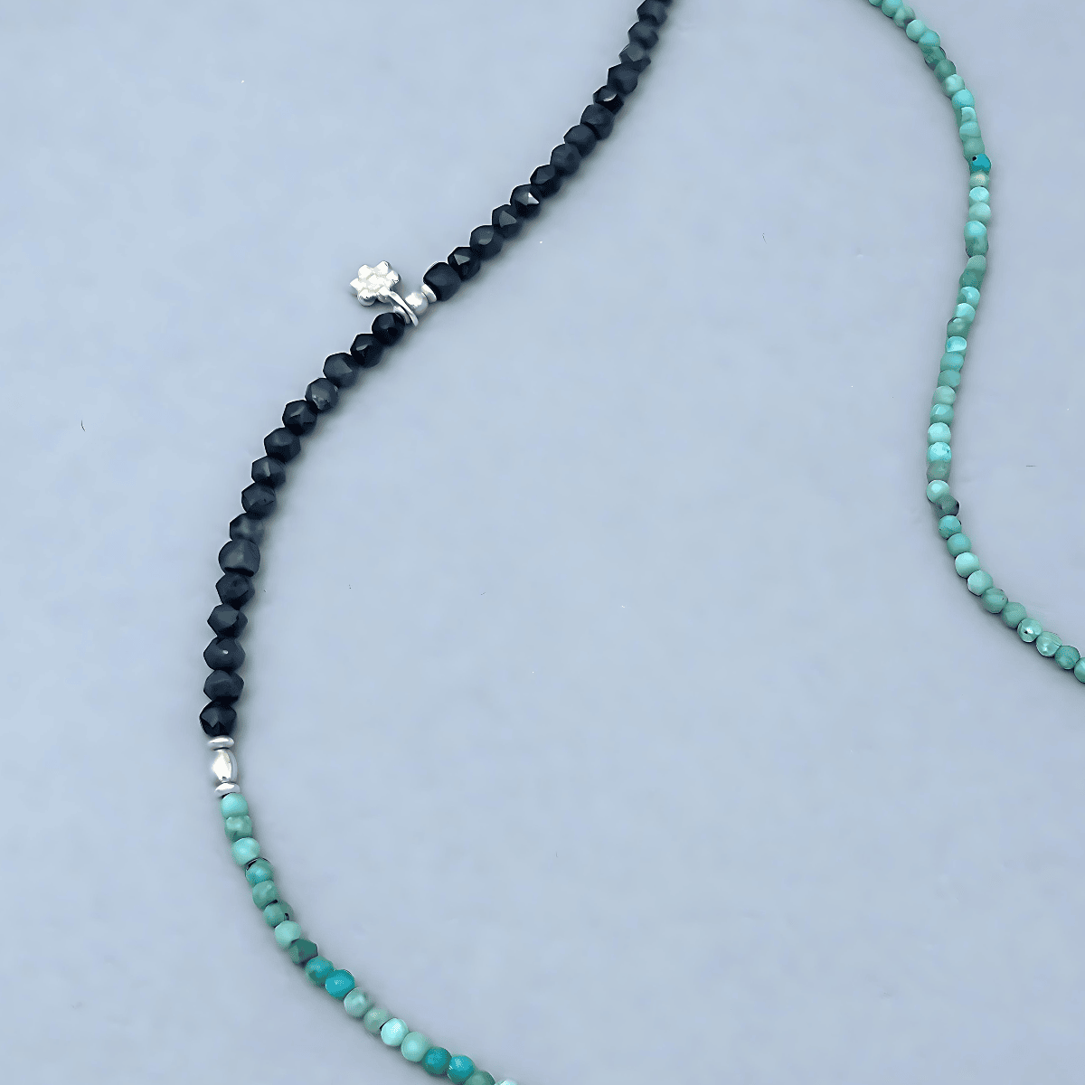 Close-up of the Le BijouBijou JOY Necklace highlighting the contrast between dark faceted Sapphire cubes and turquoise Opal beads, with a sterling silver flower charm as accent.