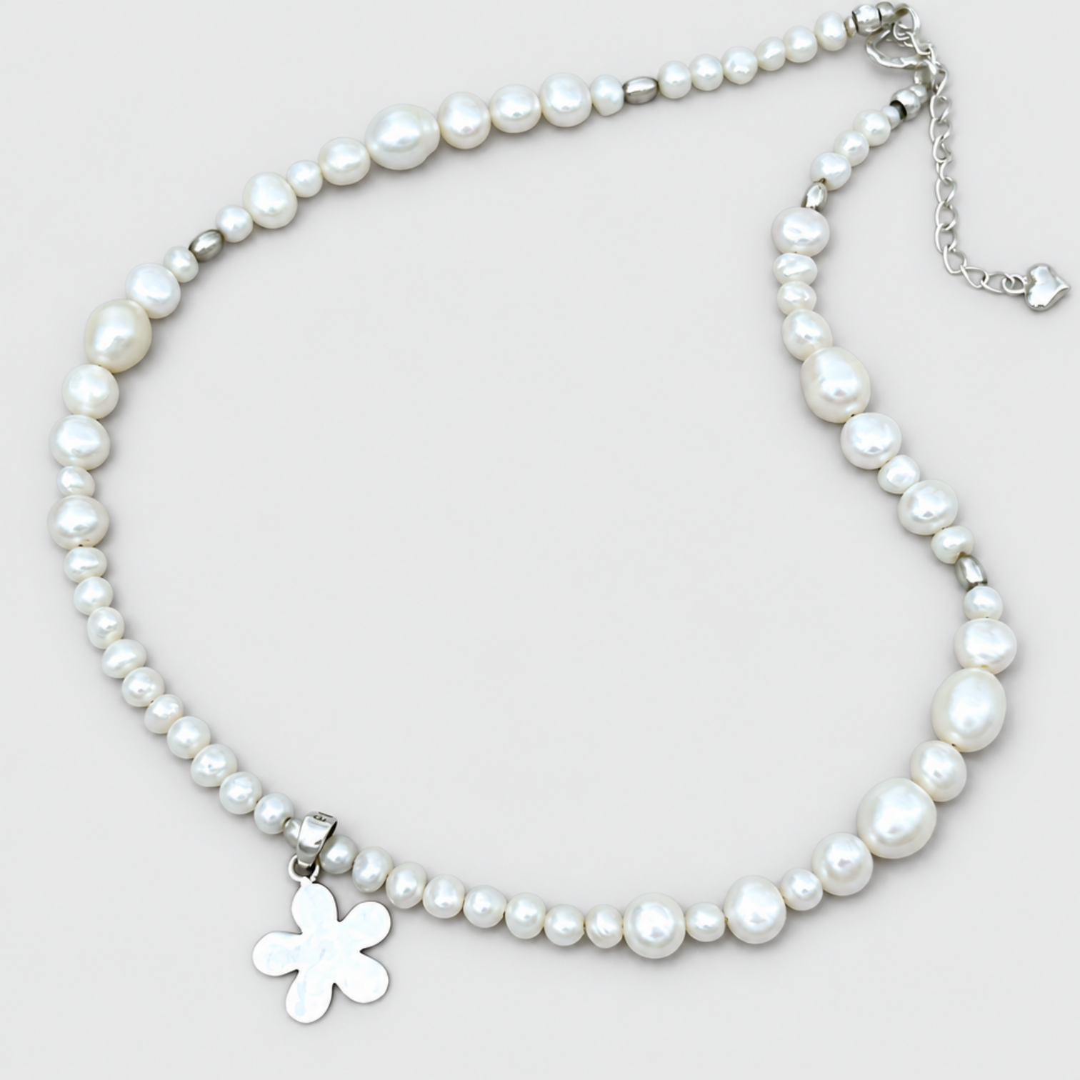 Alternative view of DAIZY white pearls with a silver-tone flower pendant at the lower left and an extension chain at the upper right on a light grey background.