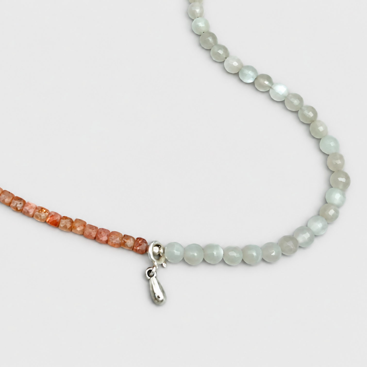 Close-up of ELLIE orange and translucent pale beads beside a silver-tone drop charm on a light grey background.