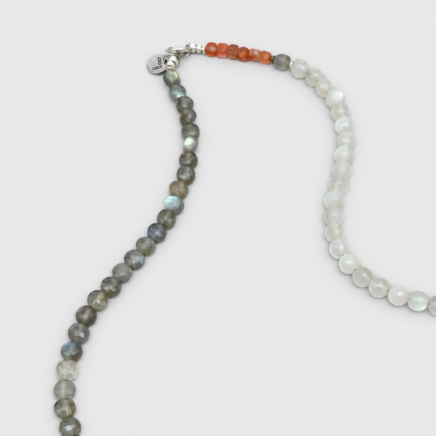 ELLIE clasp detail with a round tag, orange beads, dark grey beads and translucent pale beads on a light grey background.