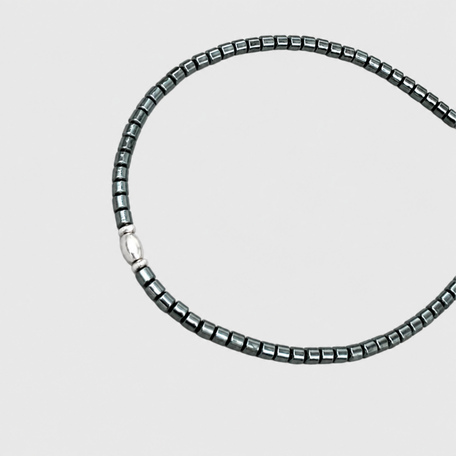 Close-up of MIDNIGHT SILVER bracelet showing dark metallic cylindrical beads and an oval silver accent with silver spacers on a neutral light-grey background.