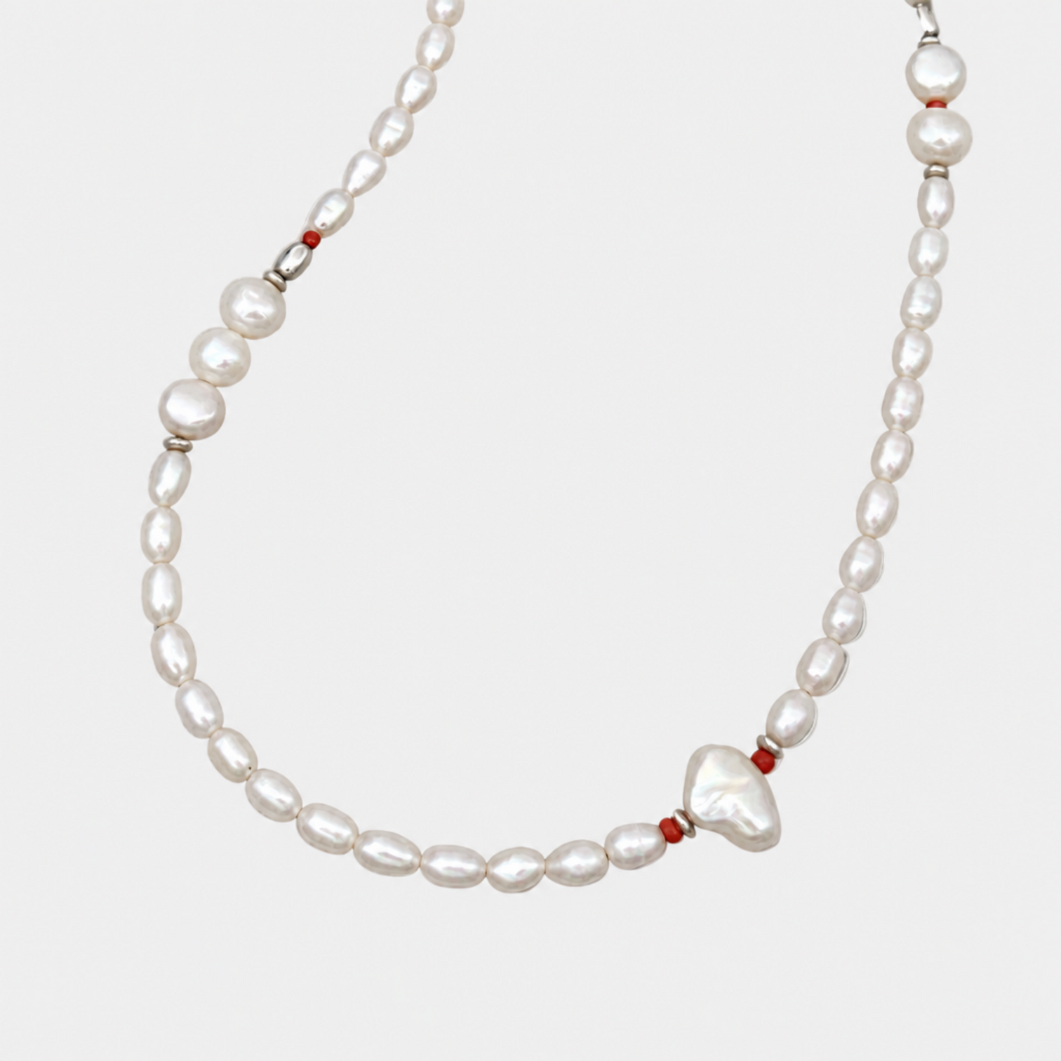 Close-up of NORA oval and round white pearls with red coral beads and a baroque pearl on a very light grey background.