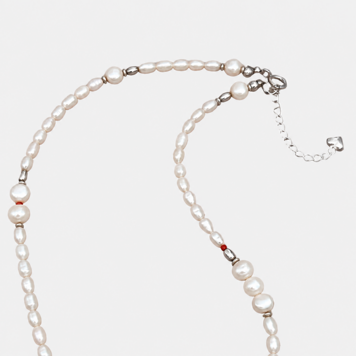 NORA white pearl necklace detail showing red coral beads, silver clasp, extension chain and charm on a light grey background.