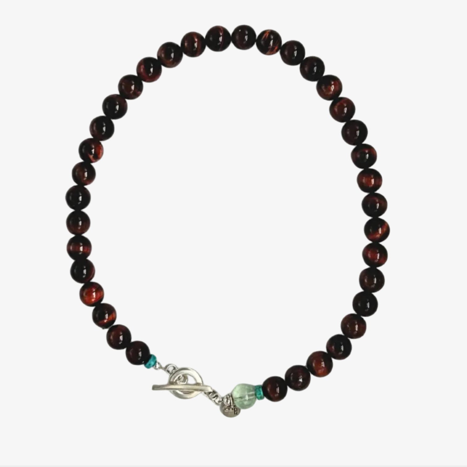 A beaded necklace of polished red-brown tiger's eye beads, with a silver toggle clasp and a fluorite bead with a silver logo charm, displayed on a very light grey neutral background. 