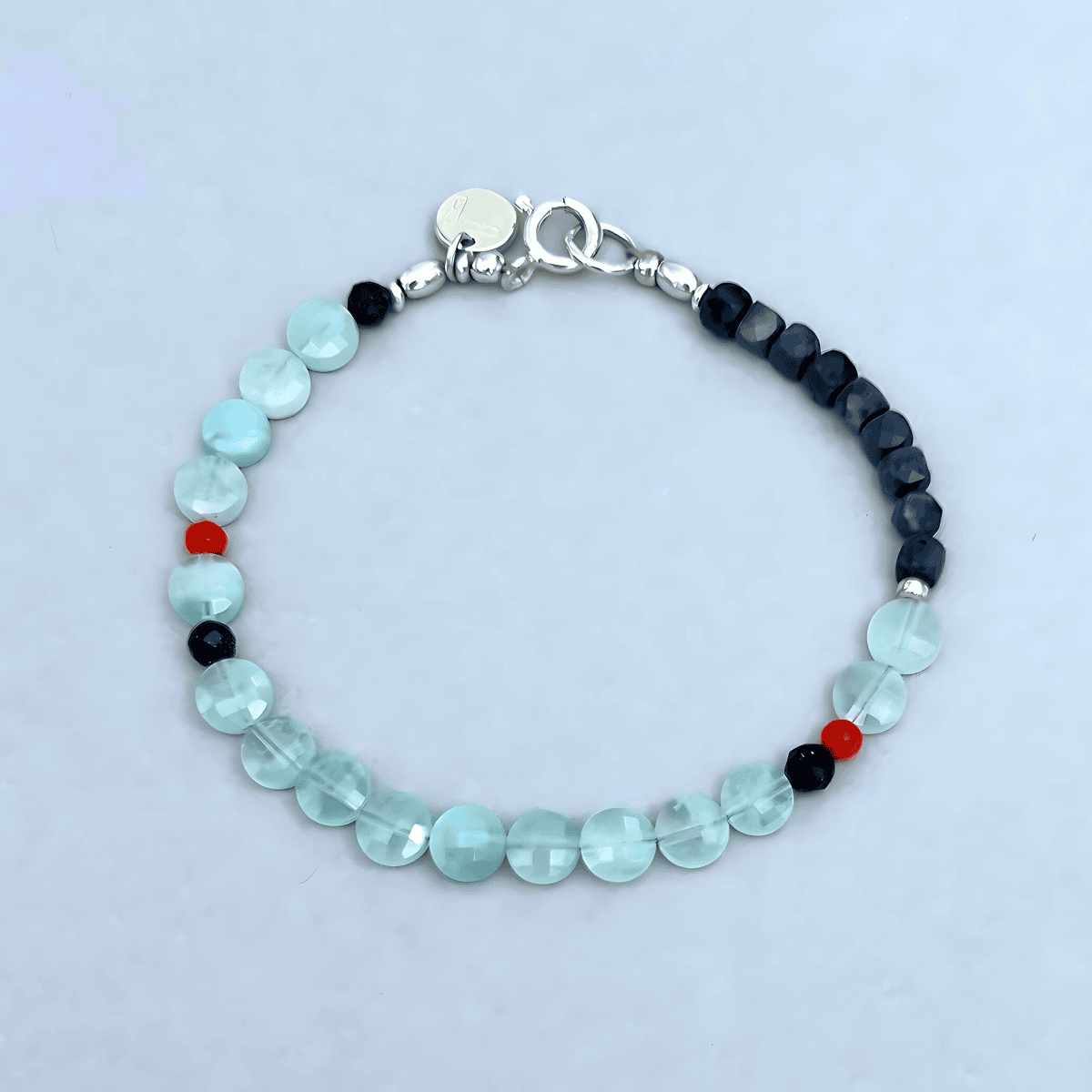 A beaded bracelet with faceted light Aquamarine beads, dark navy blue Saphires beads, and tiny red accent of coral beads, finished with a silver clasp.