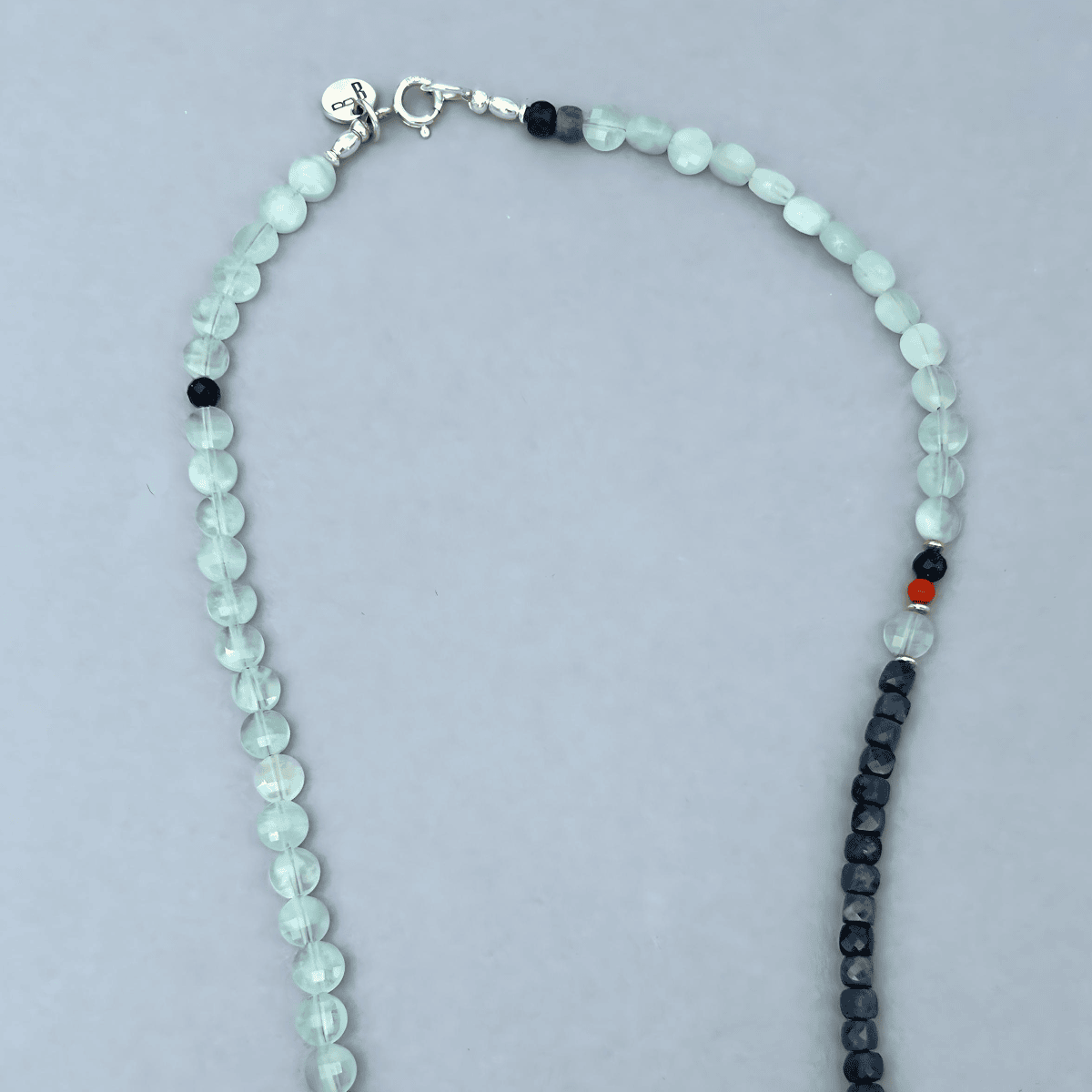 Top section of the Le BijouBijou Perfect Match Necklace showing the sterling silver clasp and charm tag, with pale Aquamarine beads, dark Sapphire cubes and a red Coral accent bead.

