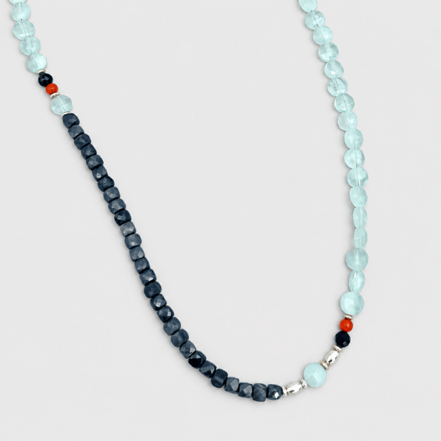 Close-up of PERFECT MATCH necklace showing pale-blue beads, dark faceted beads, red accents and silver fittings on a neutral light-grey background.