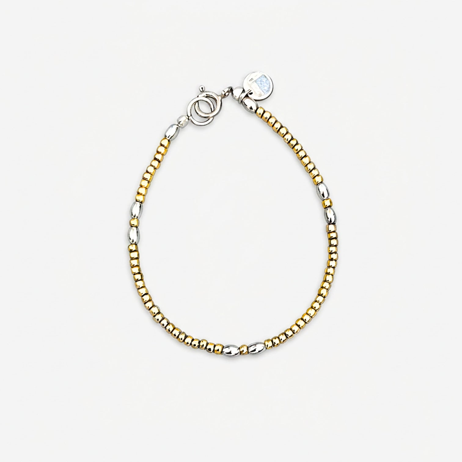 A  delicate beaded bracelet featuring alternating strands of small gold and silver beads, finished with a silver lobster clasp and a round silver tag, displayed on a neutral light gray background.
