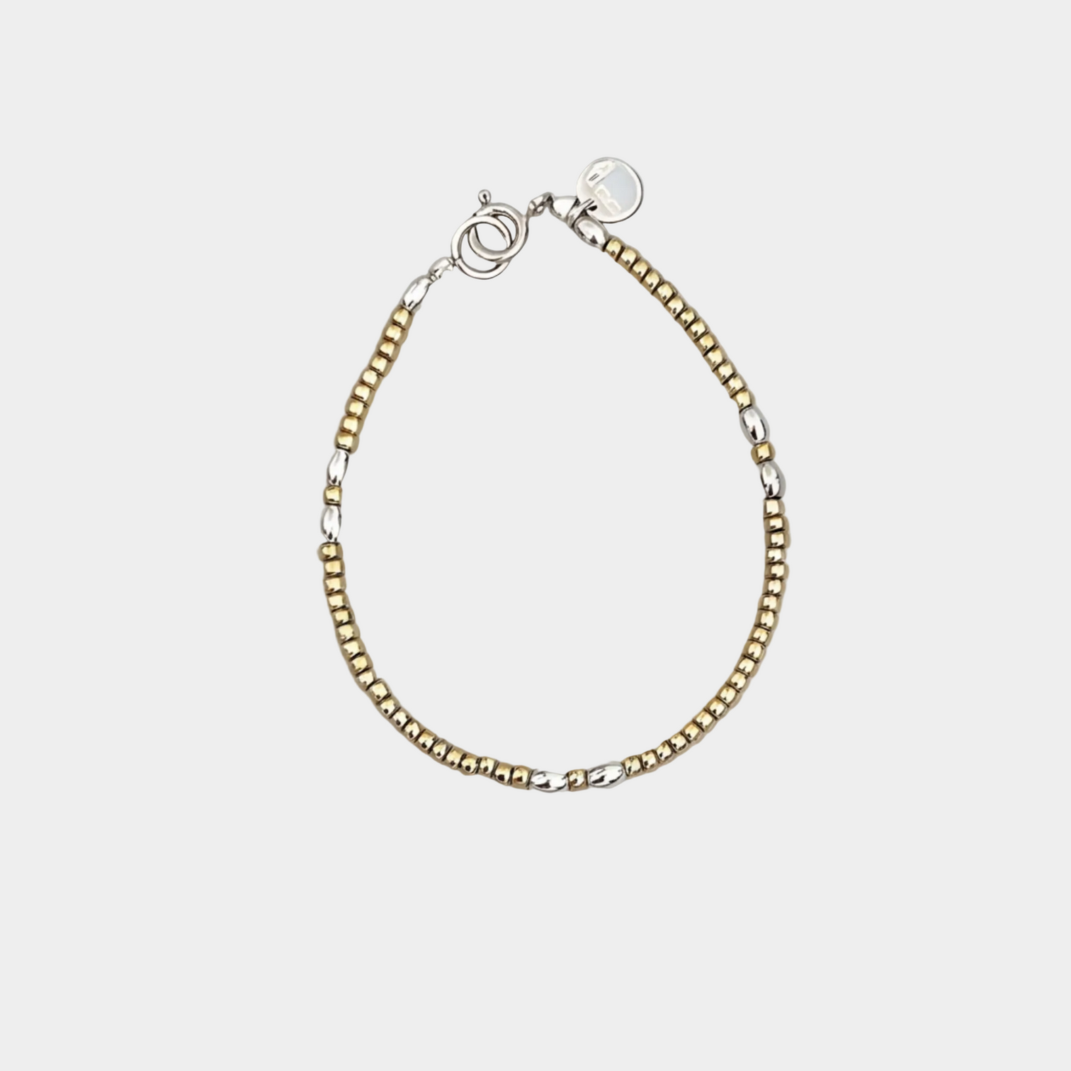A  delicate beaded bracelet featuring alternating strands of small gold and silver beads, finished with a silver lobster clasp and a round silver tag, displayed on a neutral light gray background.
