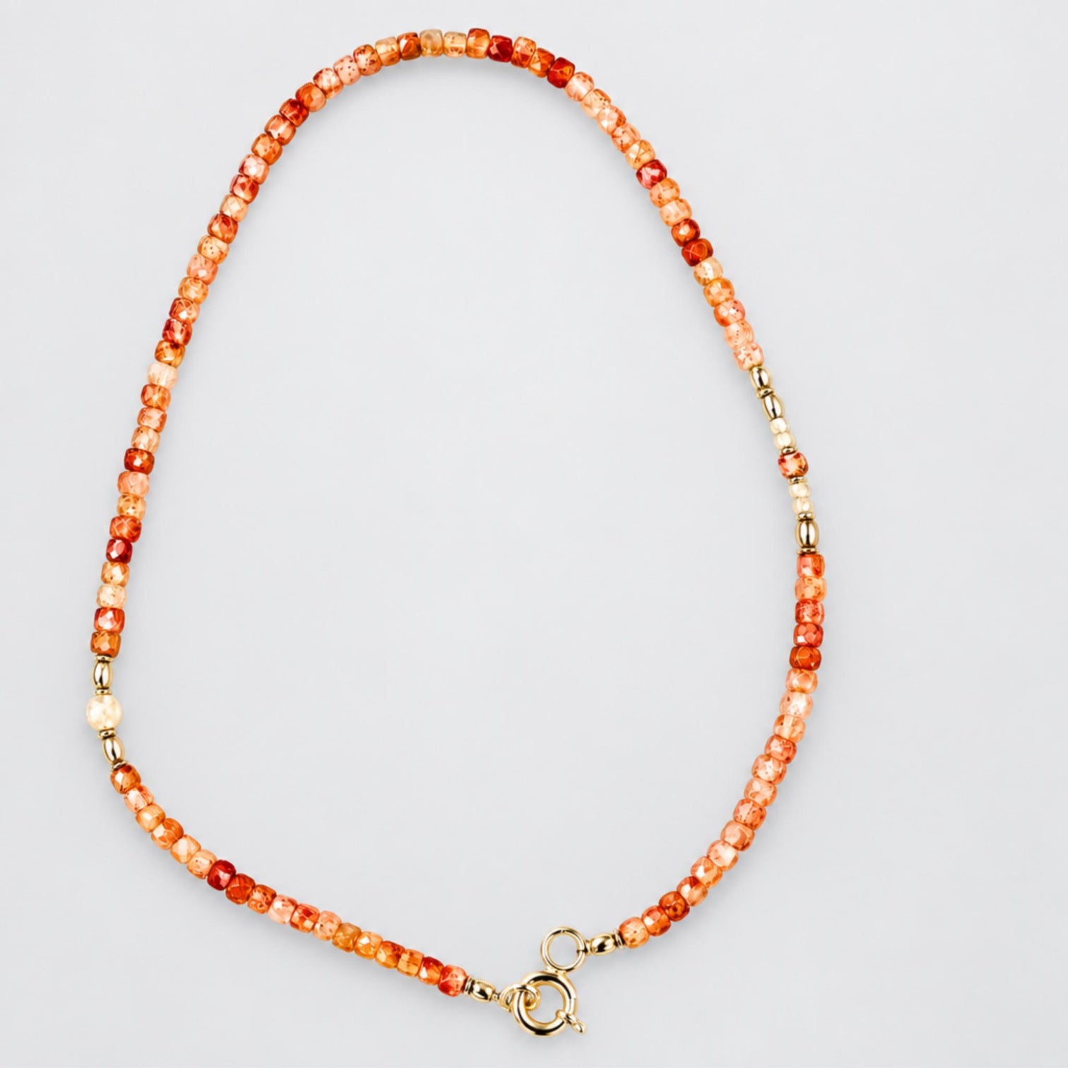 A beaded necklace with square faceted sunstone beads,  faceted moonstone bead accents, silver-toned spacers and a silver clasp, shown on a plain light grey background.