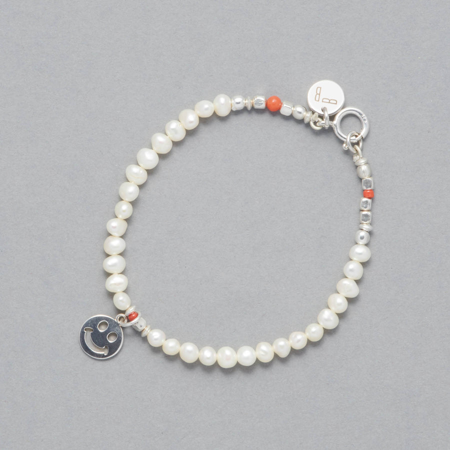 The ALAIA Bracelet is made with cultured freshwater white pearls, a sterling silver smiley charm and elements and a touch of coral. 