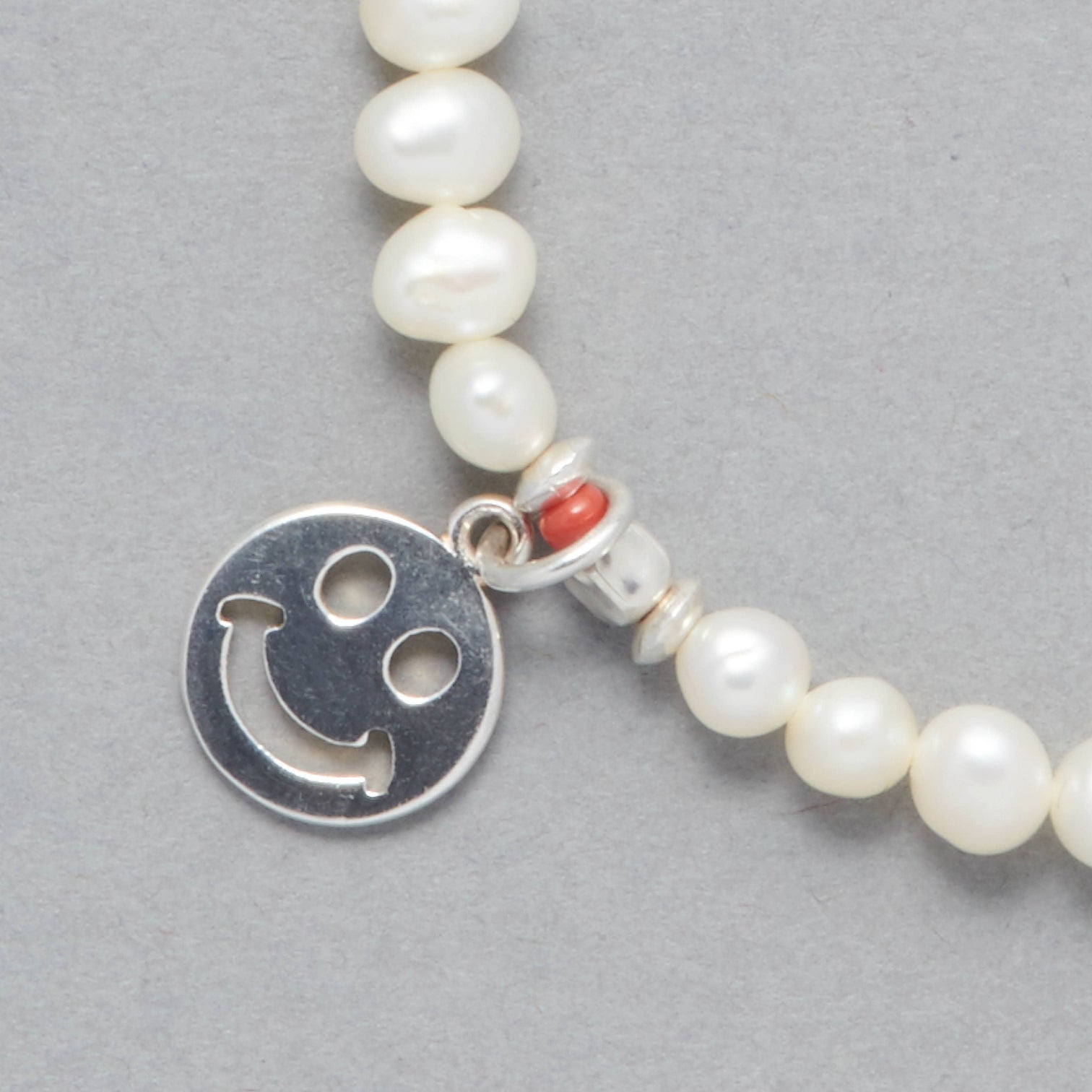 ALAIA Bracelet, close-up of the Smiley Sterling Silver Charm, the Freshwater White Pearls and the touch of Coral. 