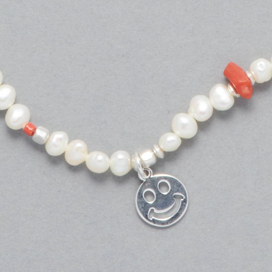 ALAIA Necklace, close-up of sterling silver smiley charm, freshwater white pears and touch of coral. Close