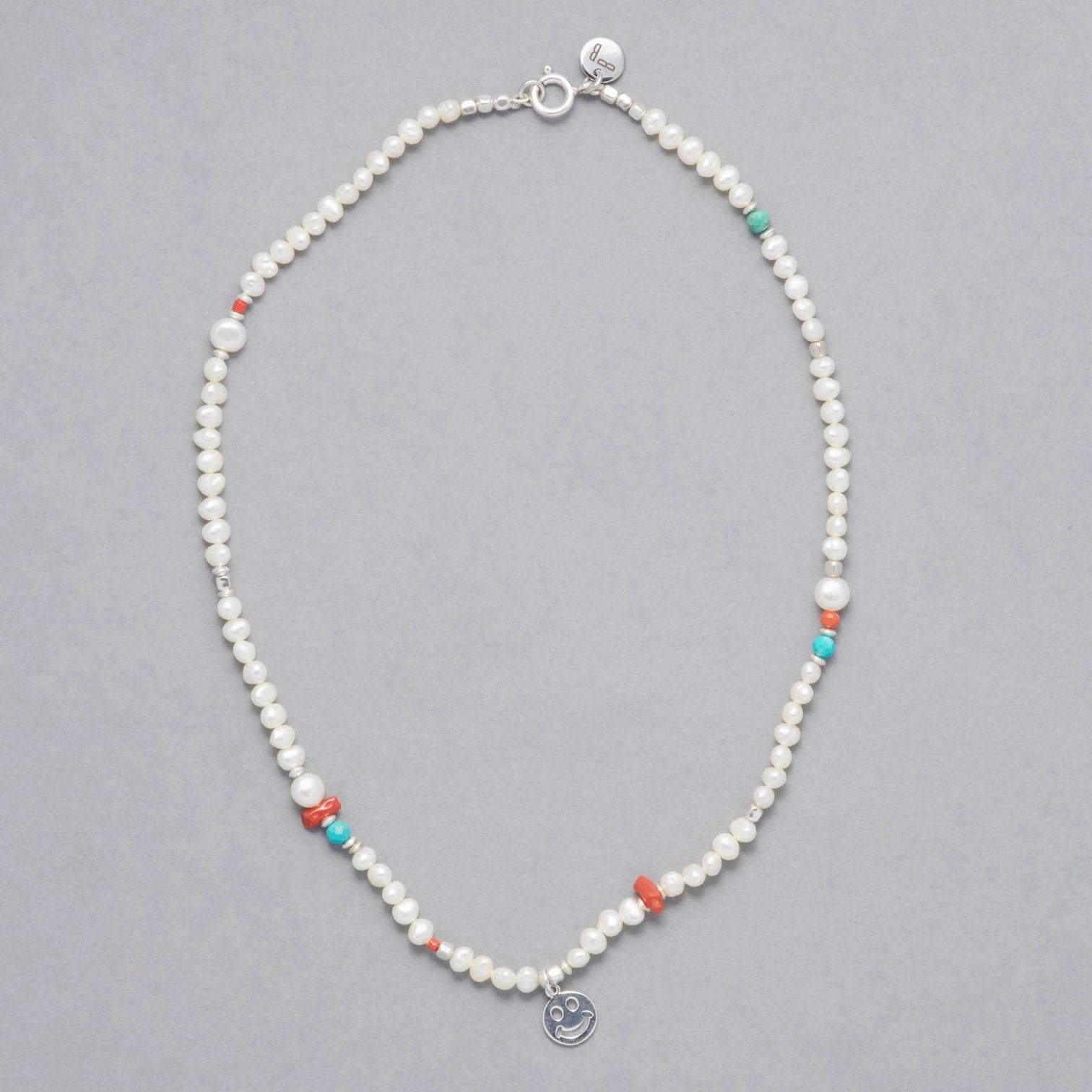 The ALAIA Necklace consists of beautiful Cultured Freshwater White Pearls and an uplifting touch of Coral and Turquoise and a Silver Sterling Smiley Charm.