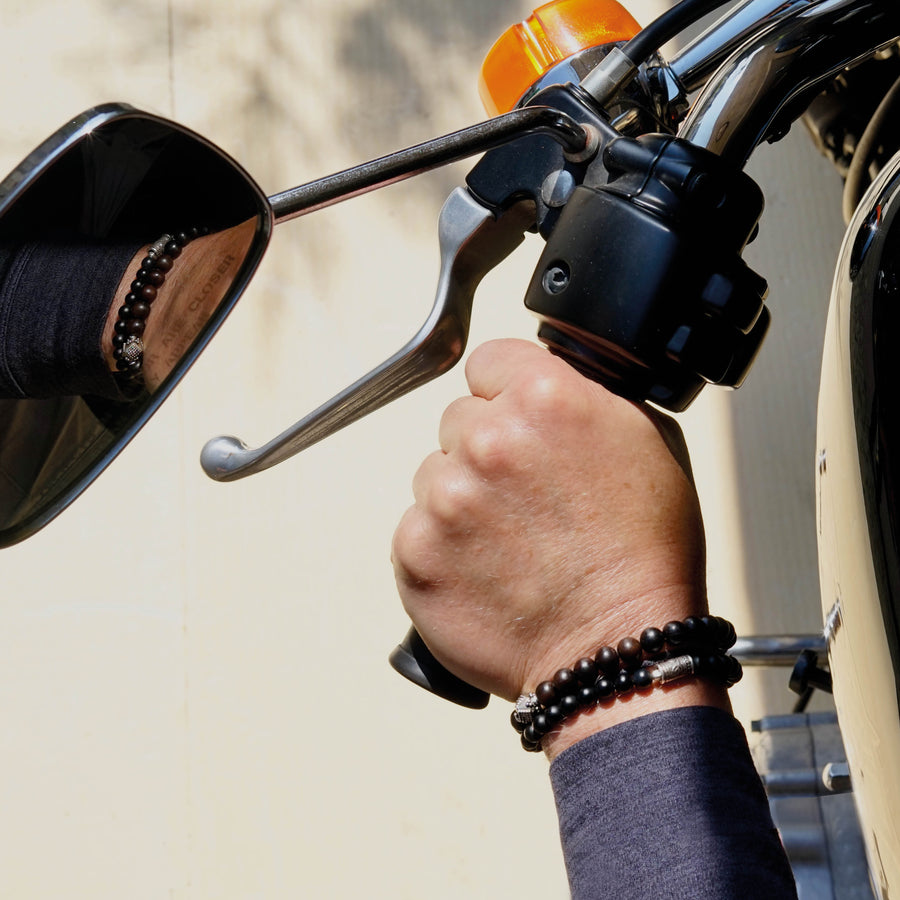 Close view of male model on a Harley Davidson Bike wearing the ALEC Men beaded bracelet made with Ebony and a sterling silver center piece and the MAXIM Men beaded bracelet made with Onyx and sterling silver elements. 