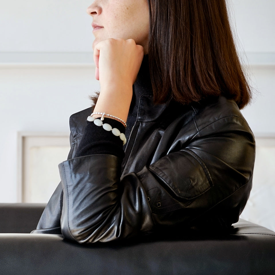 Side Shot of a female Model sitting on on couch, only part of her face is seen. She is wearing the LE BIJOUBIJOU ALINA Double Wrap Bracelet made with faceted Olive-Shaped Moonstone and Sterling Silver. Only part of her face is seen. 