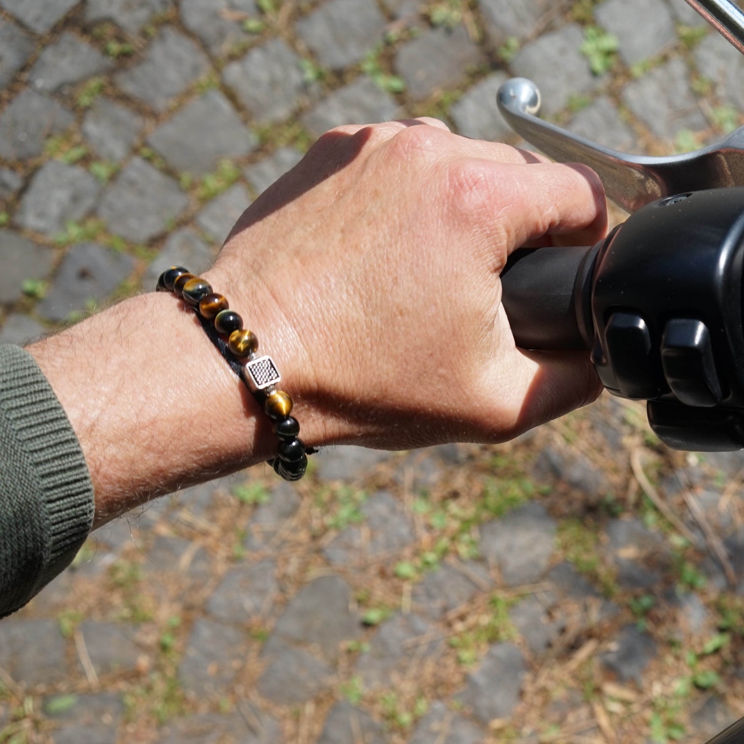 Wrist of male model on a bike. He is wearing the Chey Bracelet, a Men Beaded Bracelet made with Blue Tiger Eye and a Sterling Silver Element.
