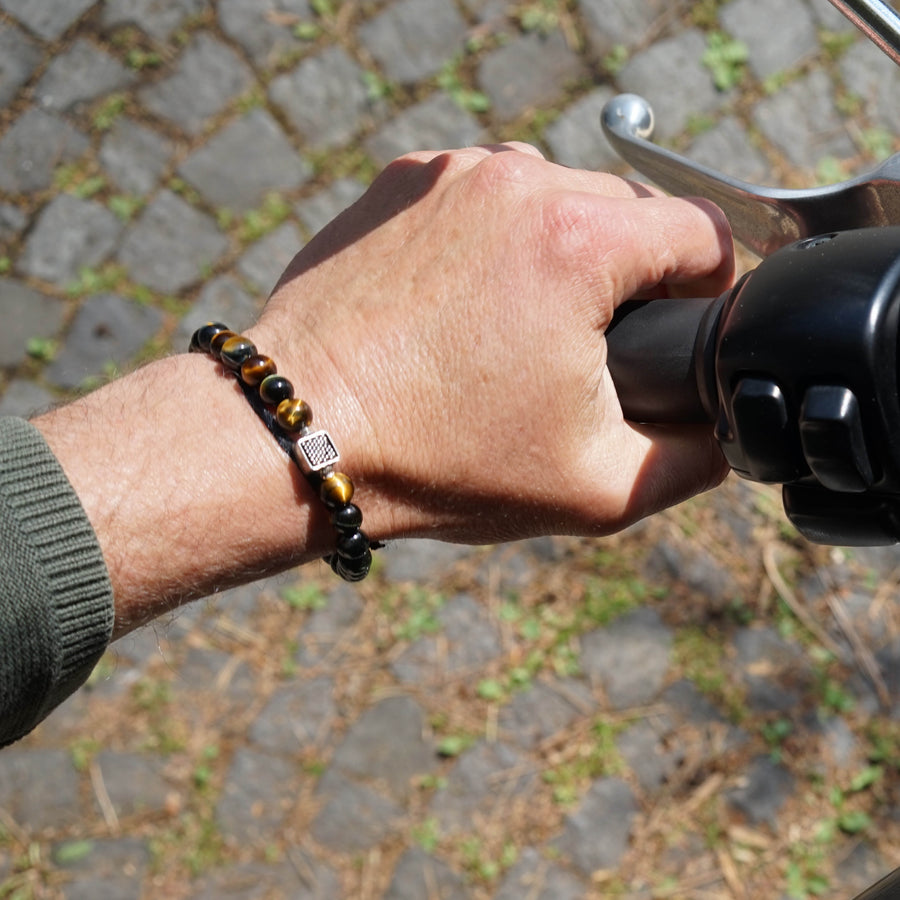 Wrist of male model on a bike. He is wearing the Chey Bracelet, a Men Beaded Bracelet made with Blue Tiger Eye and a Sterling Silver Element.