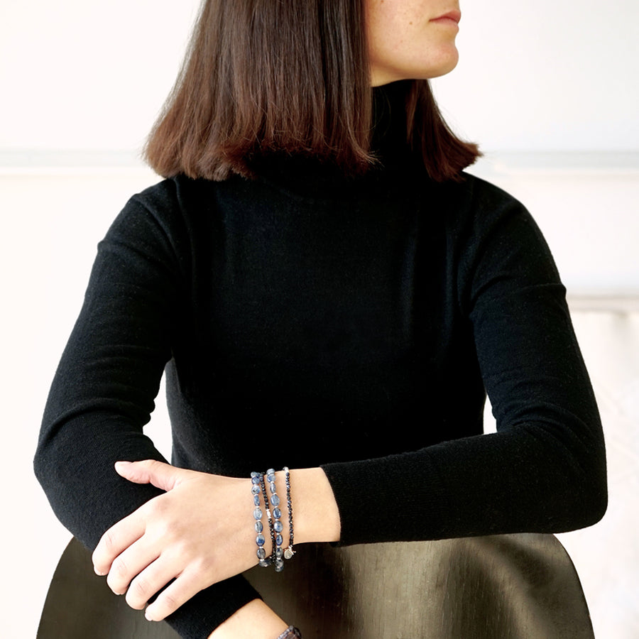 Image of a female model siting on a chair. Only part of her face is visible. She is wearing the LE BIJOUBIJOU CIEL Double Wrap Bracelet made with oval-shaped Kyanite, faceted Sapphires and Sterling Silver.