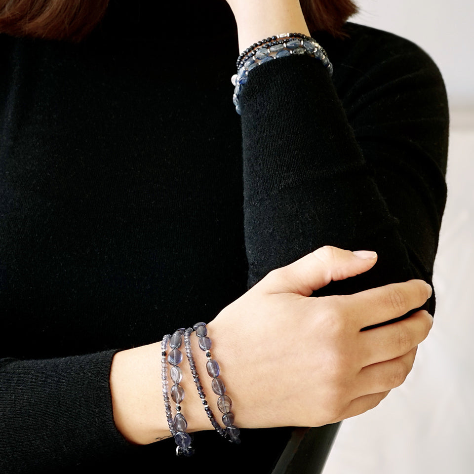 Close-up of a female model's arm. She is wearing the LE BIJOUBIJOU MIRA Double Wrap Bracelet made with oval-shaped Iolite and faceted Iolite. 