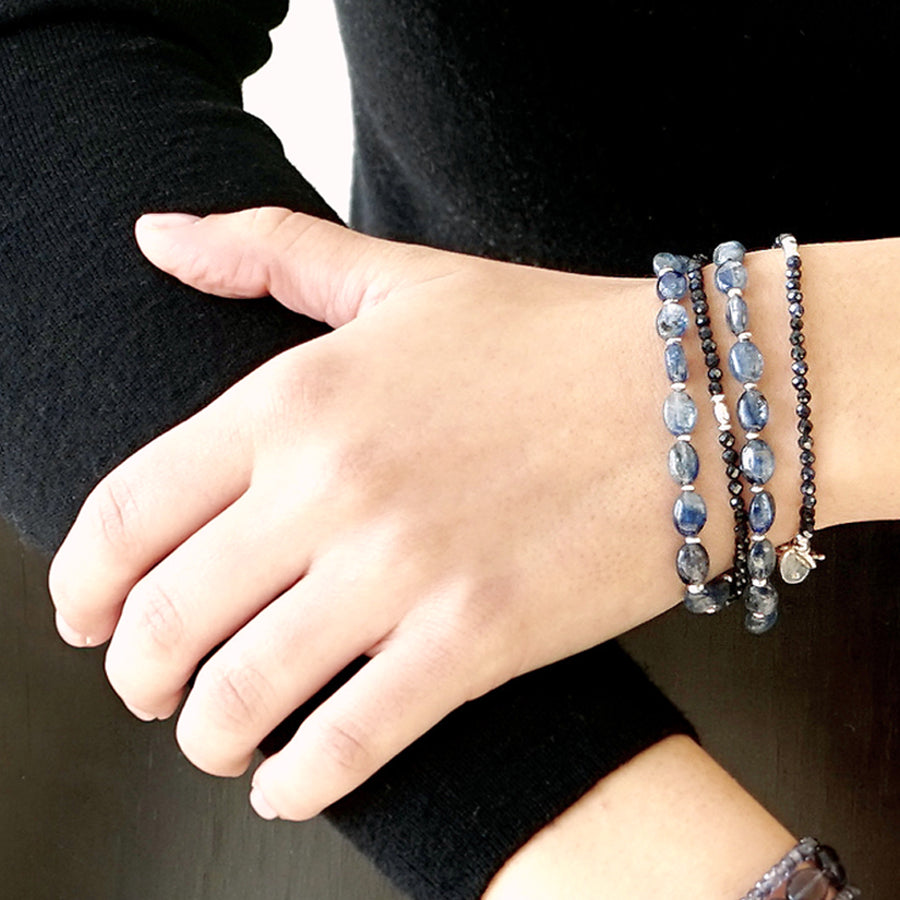 Close-up of a female model siting on a chair.  She is wearing the LE BIJOUBIJOU CIEL Double Wrap Bracelet made with oval-shaped Kyanite, faceted Sapphires and Sterling Silver.