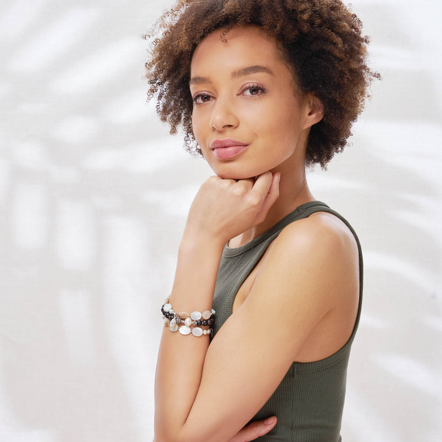 Female model is wearing the Ebony Bracelet made with Ebony Wood and Sterling Silver, and two Marilla Bracelets made with Mother of Pearl, Sterling Silver elements and charm. 