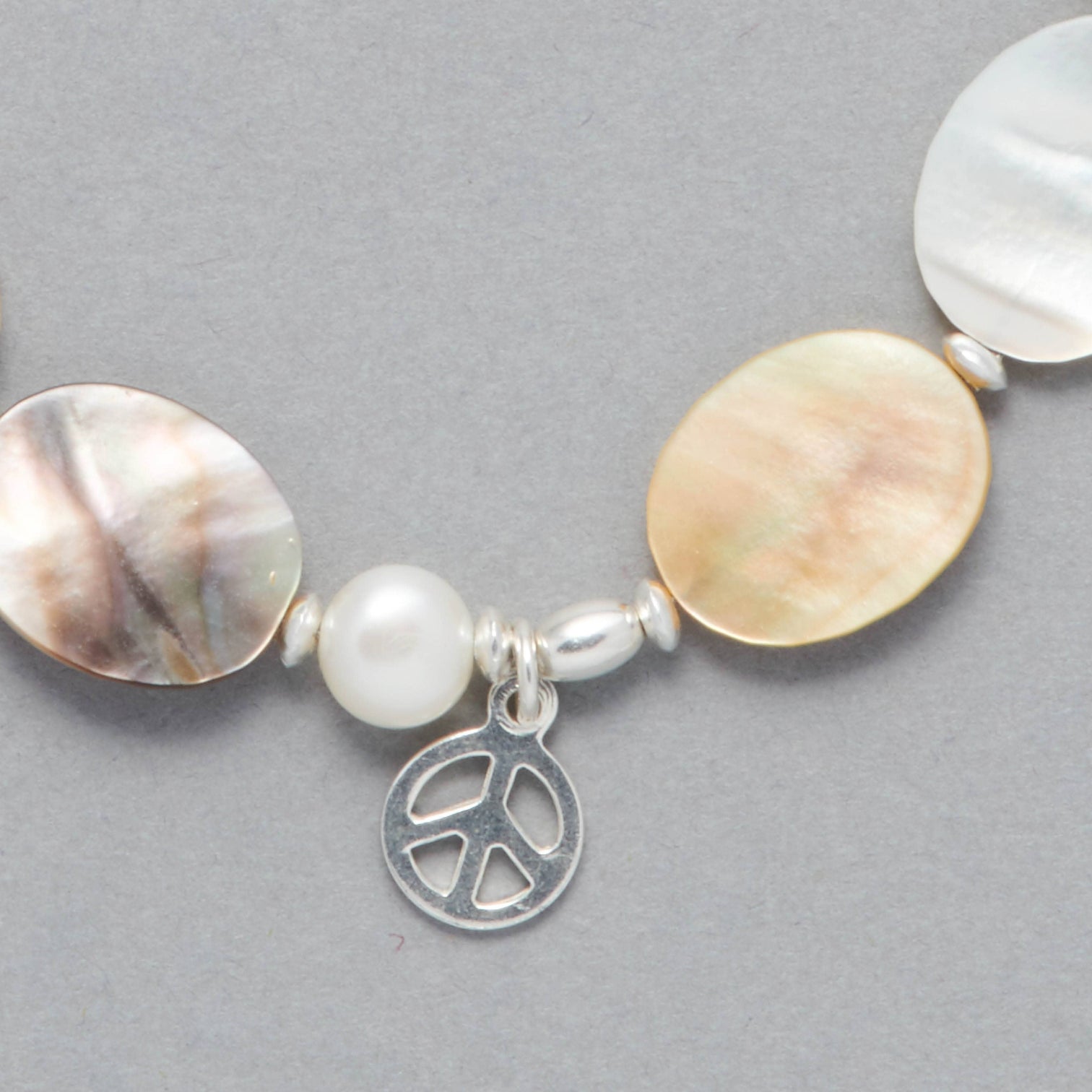 Detail shot of the Marilla Anklet made with Mother of Pearl, Freshwater White Pearls, Sterling Silver elements and a Sterling Silver Peace Symbol Charm. 