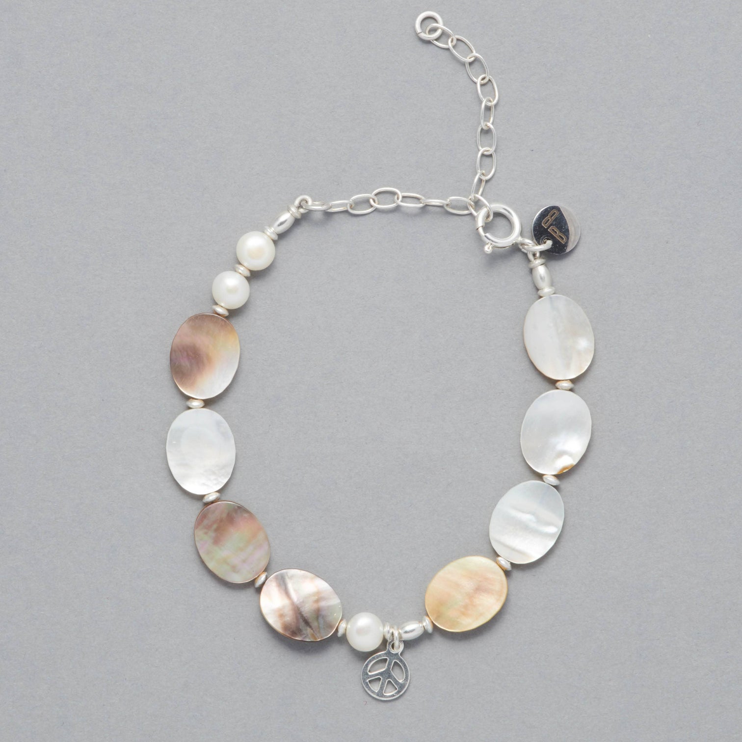 Product shot of the Marilla Anklet made with Mother of Pearl, Freshwater White Pearls, Sterling Silver elements and a Sterling Silver Peace Symbol Charm. A little silver chain allows the adjusting of the size. 