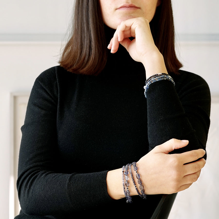 Front view of a Female Model. Her upper body with only part of her face are visible. She is wearing the LE BIJOUBIJOU MIRA Double Wrap Bracelet made with oval-shaped Iolite and faceted Iolite. 