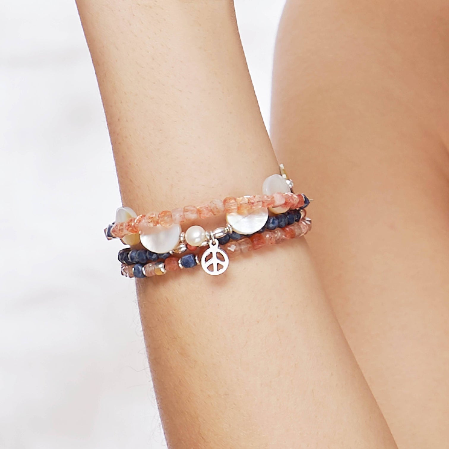 Close-Up of the female Model wearing the Sky Bracelet made with faceted square Sapphires, the Ginger Bracelet made with faceted square Sunstones and the Marilla Bracelet made with Mother of Pearls and a Sterling Silver Peace charm. 