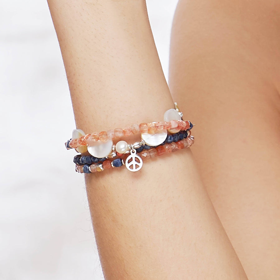 Close-Up of the female Model wearing the Sky Bracelet made with faceted square Sapphires, the Ginger Bracelet made with faceted square Sunstones and the Marilla Bracelet made with Mother of Pearls and a Sterling Silver Peace charm. 