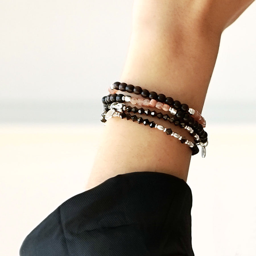 Close-up of a female model's wrist. She is wearing the SUNNY LE BIJOUBIJOU Double Wrap Bracelet made with Ebony, Sunstones and Sterling Silver and the BRONZY Double Wrap Bracelet, made with Swarovski Crystals and Sterling Silver.